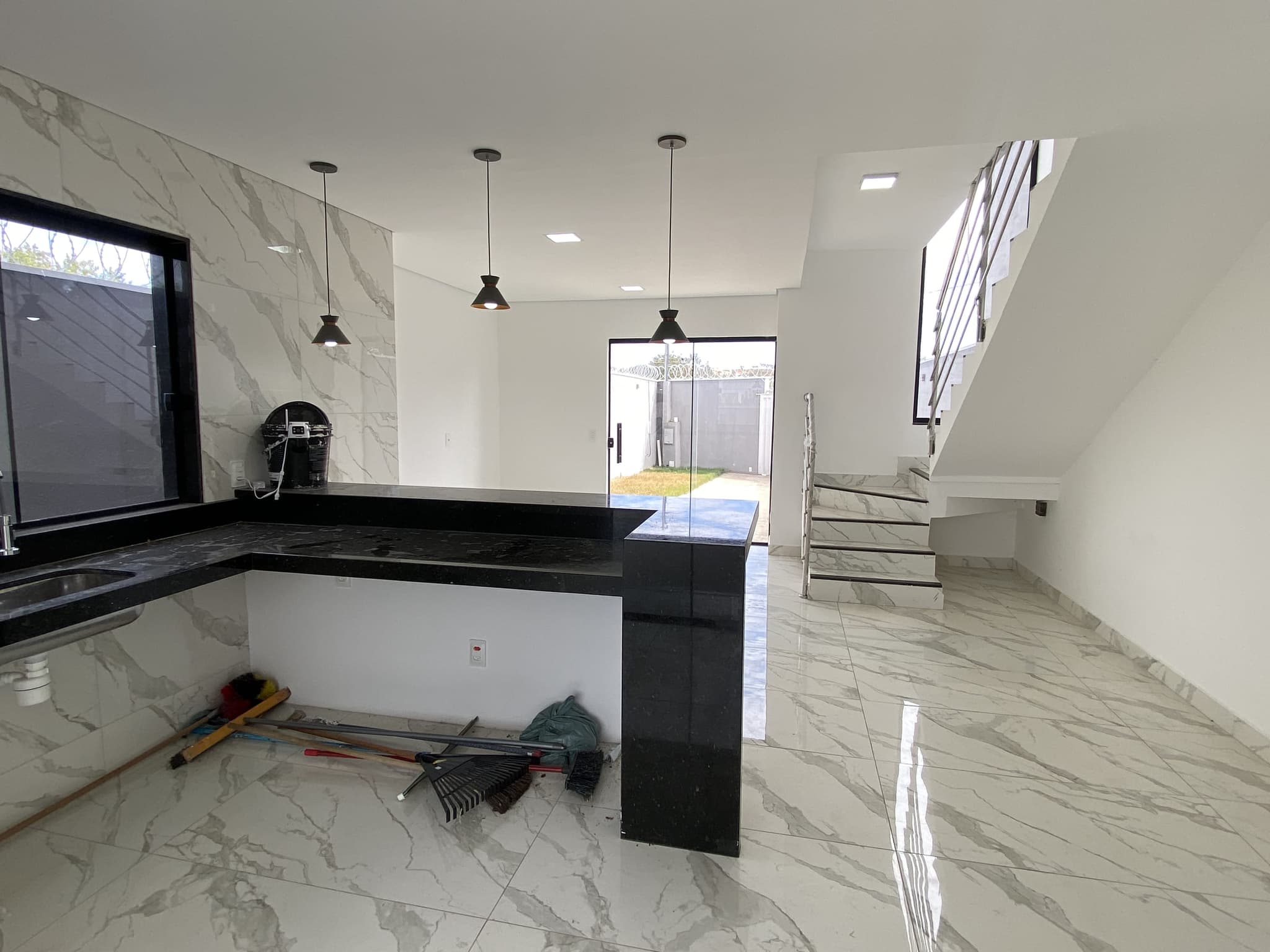 Cozinha integrada ao ambiente de convivência, com bancada em granito preto, pendentes e passagem de vidro para a área externa.