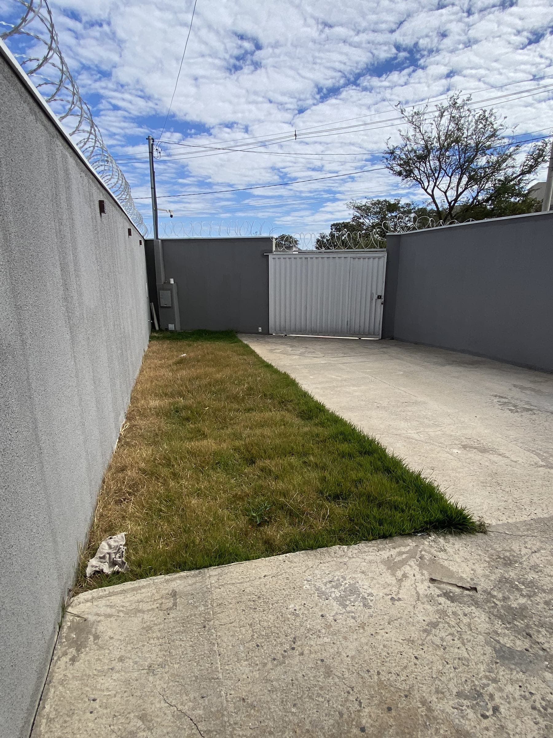 Área de garagem em concreto com faixa gramada lateral e portão de acesso ao lote.