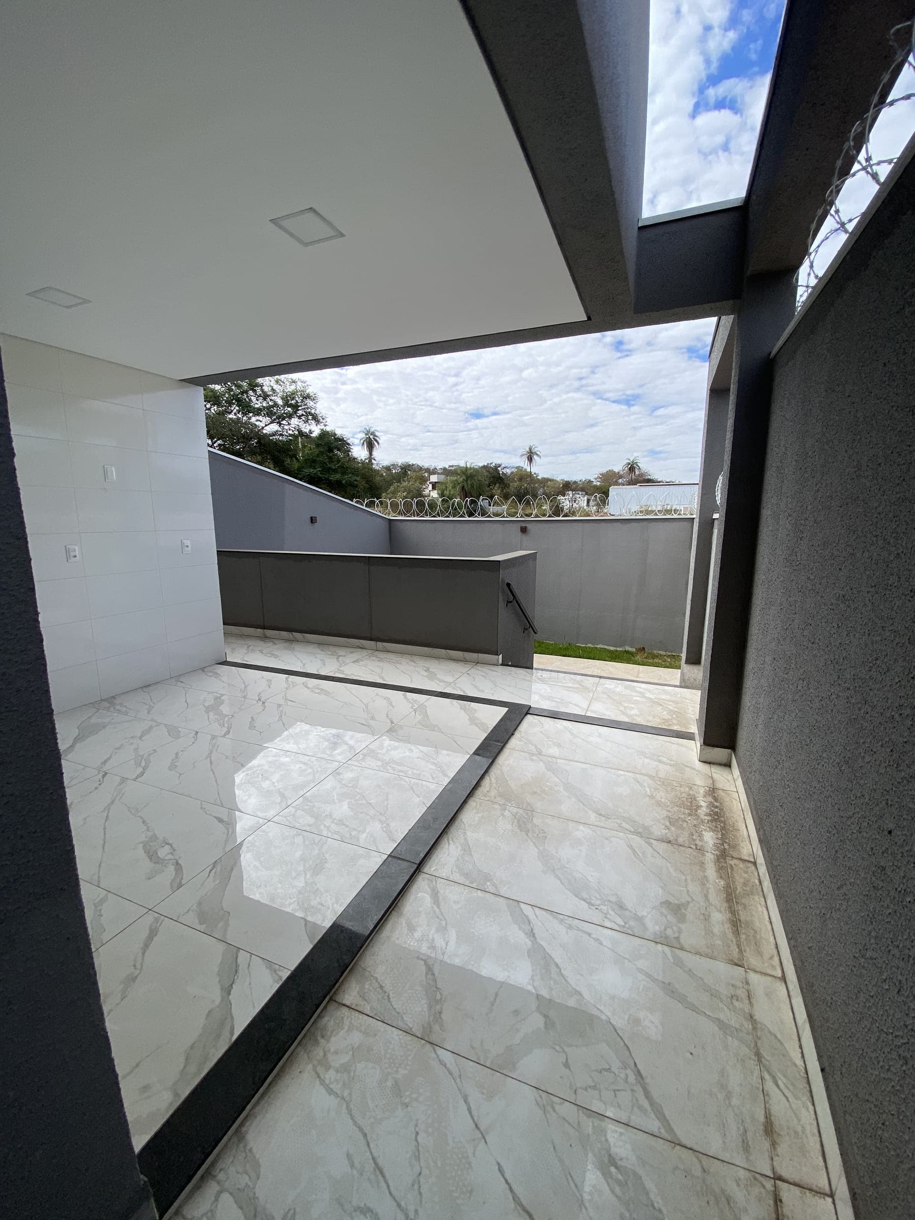 Espaço externo coberto, com bancada construída e vista aberta para a vegetação ao fundo.